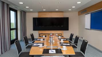 A conference room with a large table, chairs, a flat-screen TV, and a projector screen.