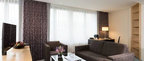 A modern hotel room with a sofa, armchair, and a small table with a vase of flowers.