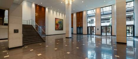 A spacious lobby with a polished floor, a staircase, and a large column with a chandelier.