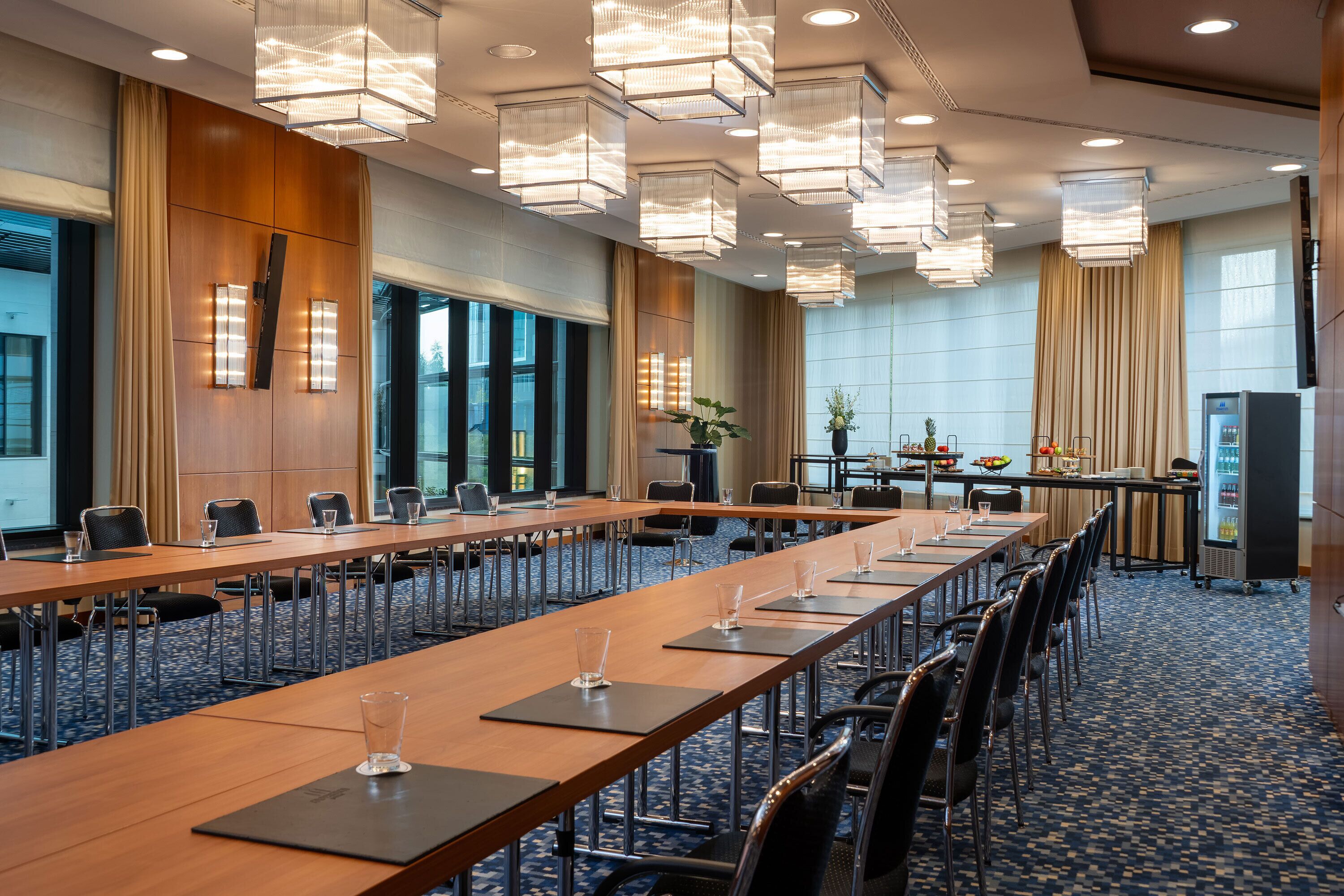 Een congreszaal met lange tafels, stoelen en moderne verlichtingsarmaturen.