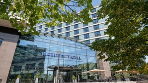 Una entrada de hotel moderna con fachada de vidrio, asientos al aire libre y una escalera que conduce a la entrada.