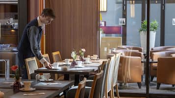A hotel dining area with tables set for service, a reception desk, and a large potted plant.