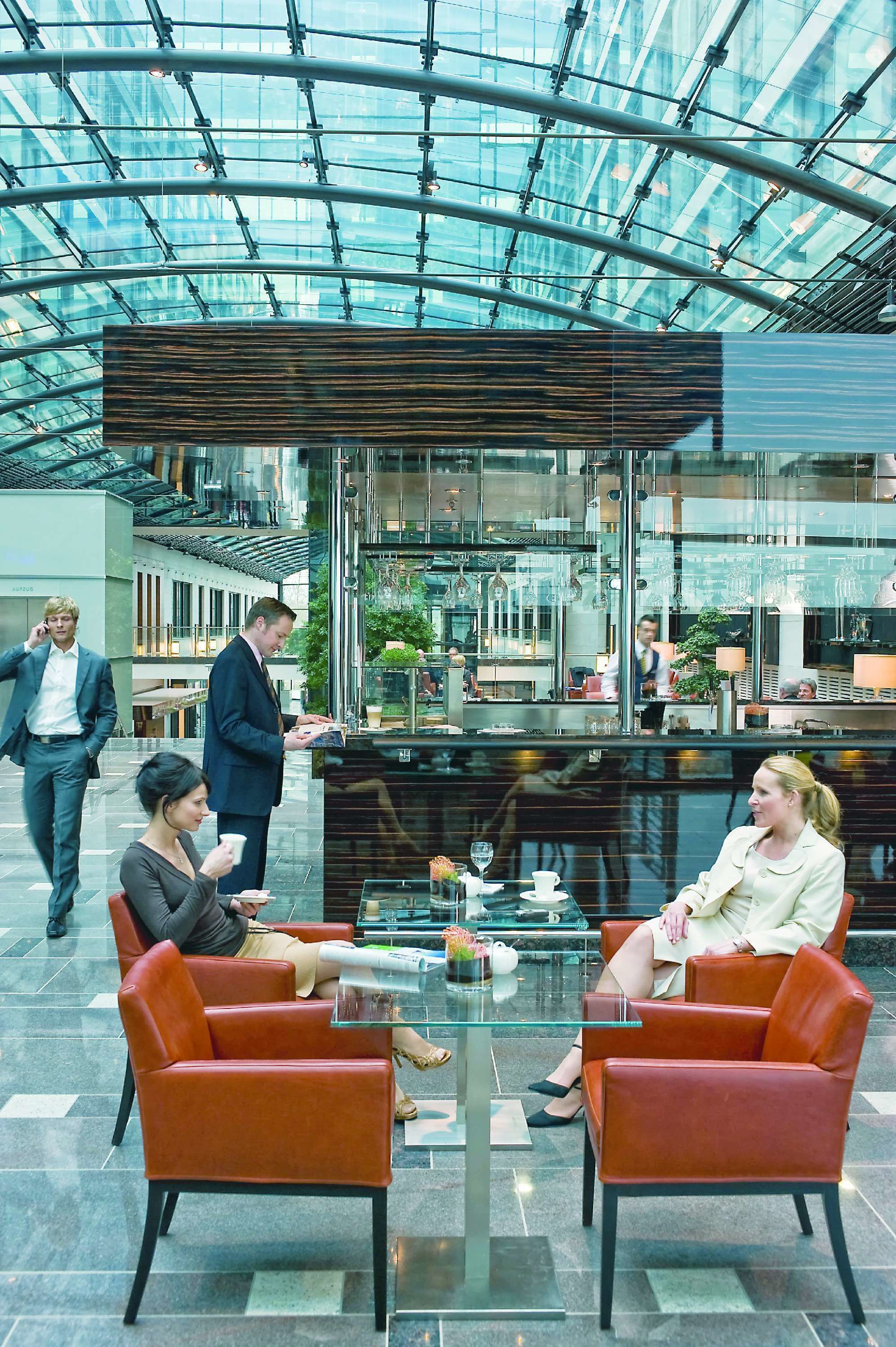 A modern indoor space with a glass ceiling, red chairs, and a central table.