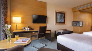 Ein Hotelzimmer mit Schreibtisch, Stuhl, Flachbildfernseher, Bett und einem kleinen Tisch mit Zeitschrift und Glas Orangensaft.