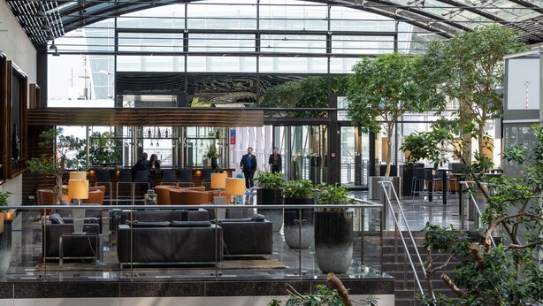 Un moderno vestíbulo de hotel con techo de vidrio, zonas de estar e instalaciones de plantas de interior.
