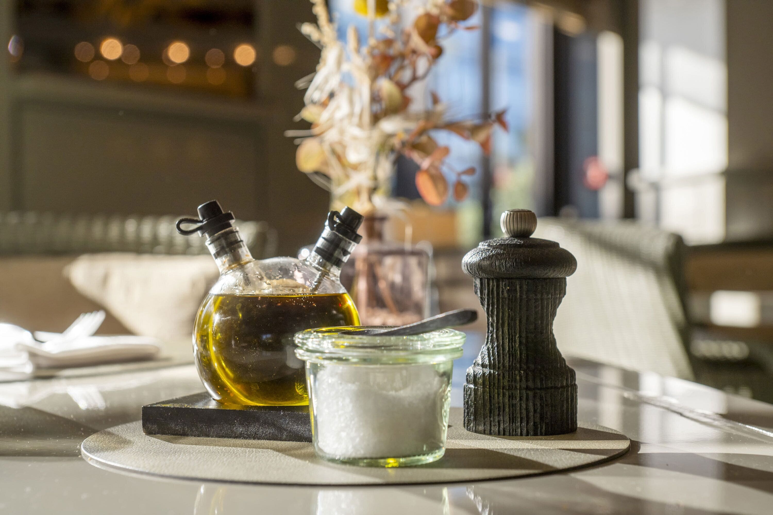 A table with a bottle of olive oil, a jar of salt, and a pepper grinder.