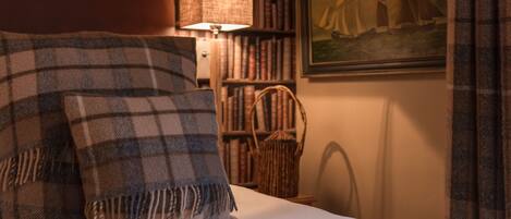 Een bed met een geruite deken en kussens, een lamp, een boekenplank en een schilderij van een zeilboot.