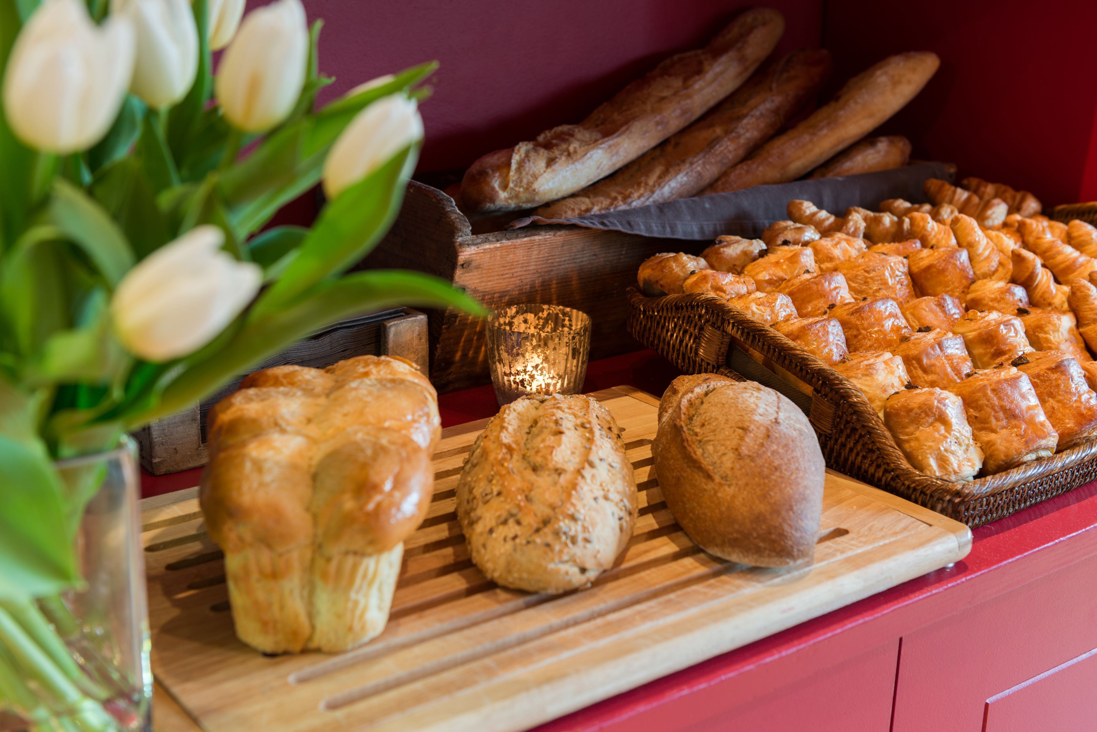 A variety of baked goods on a wooden board, including croissants and bread, with a candle in the background.