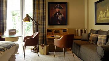 A room with a wooden desk, two leather chairs, a brown sofa, a framed portrait, and a window with curtains.