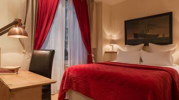 A hotel room with a bed, a desk, a chair, a lamp, and a painting on the wall.