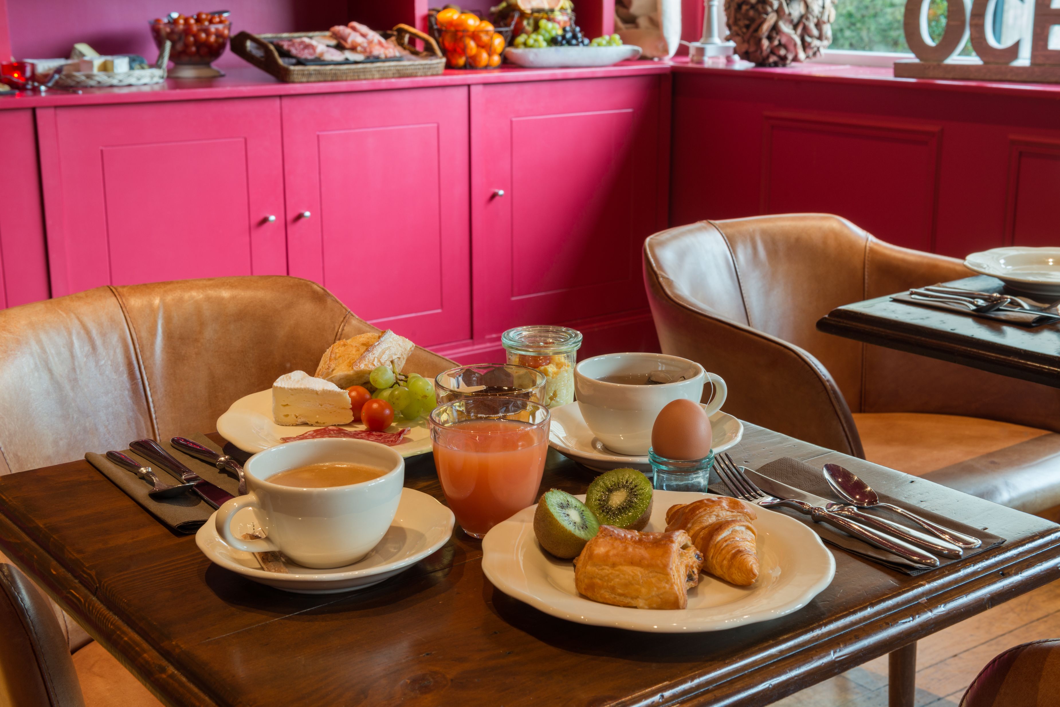 Een ontbijttafel gedekt voor twee personen, met borden vol croissants, fruit en een glas sap.