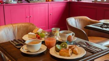 Een ontbijttafel gedekt voor twee personen, met borden vol croissants, fruit en een glas sap.