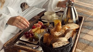 Una habitación acogedora con una estantería, un cuadro y una bandeja de desayuno con pan, fruta y una cafetera.