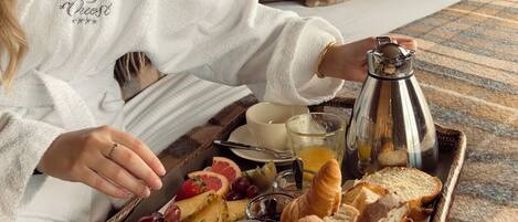 A cozy room with a bookshelf, a painting, and a breakfast tray with bread, fruit, and a coffee pot.