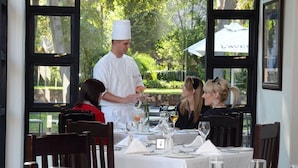 Un restaurante con terraza, un chef sirviendo un plato y una mesa preparada para cuatro personas.