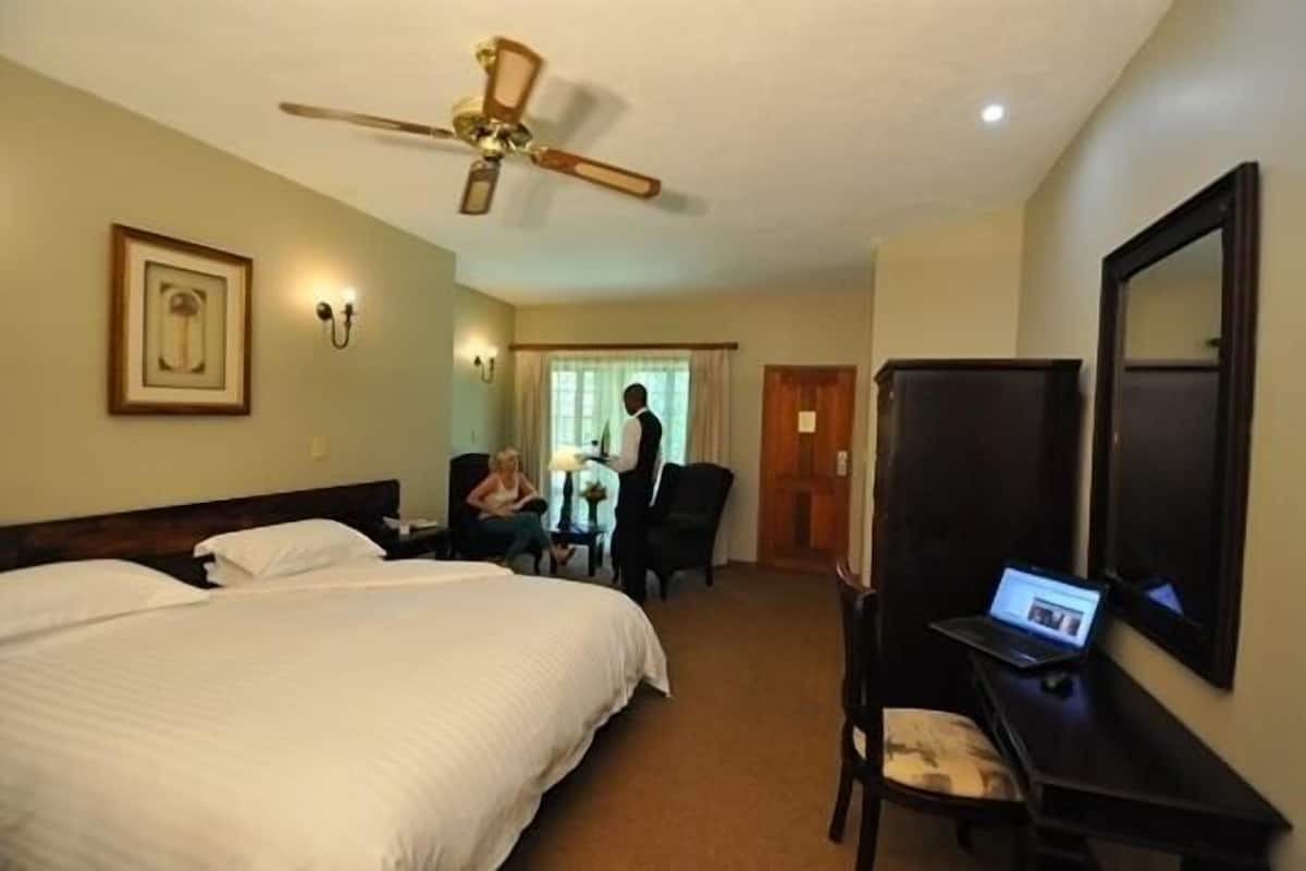 Habitación de hotel con cama, escritorio con computadora portátil, ventilador de techo y un cuadro en la pared.