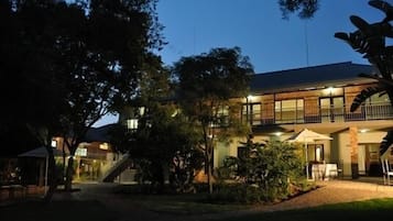 A two-story building with a balcony on the upper floor, surrounded by trees and a well-maintained garden.