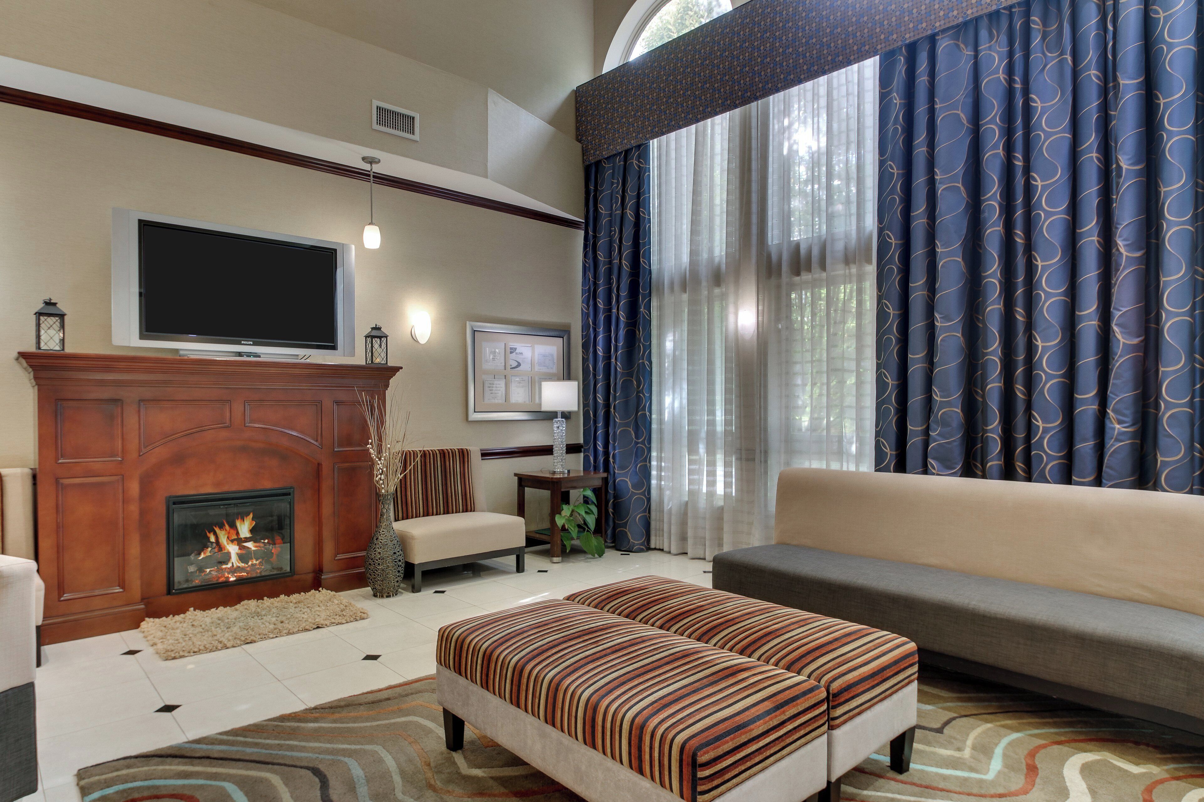 A living room with a fireplace, a television, a sofa, and a patterned ottoman.