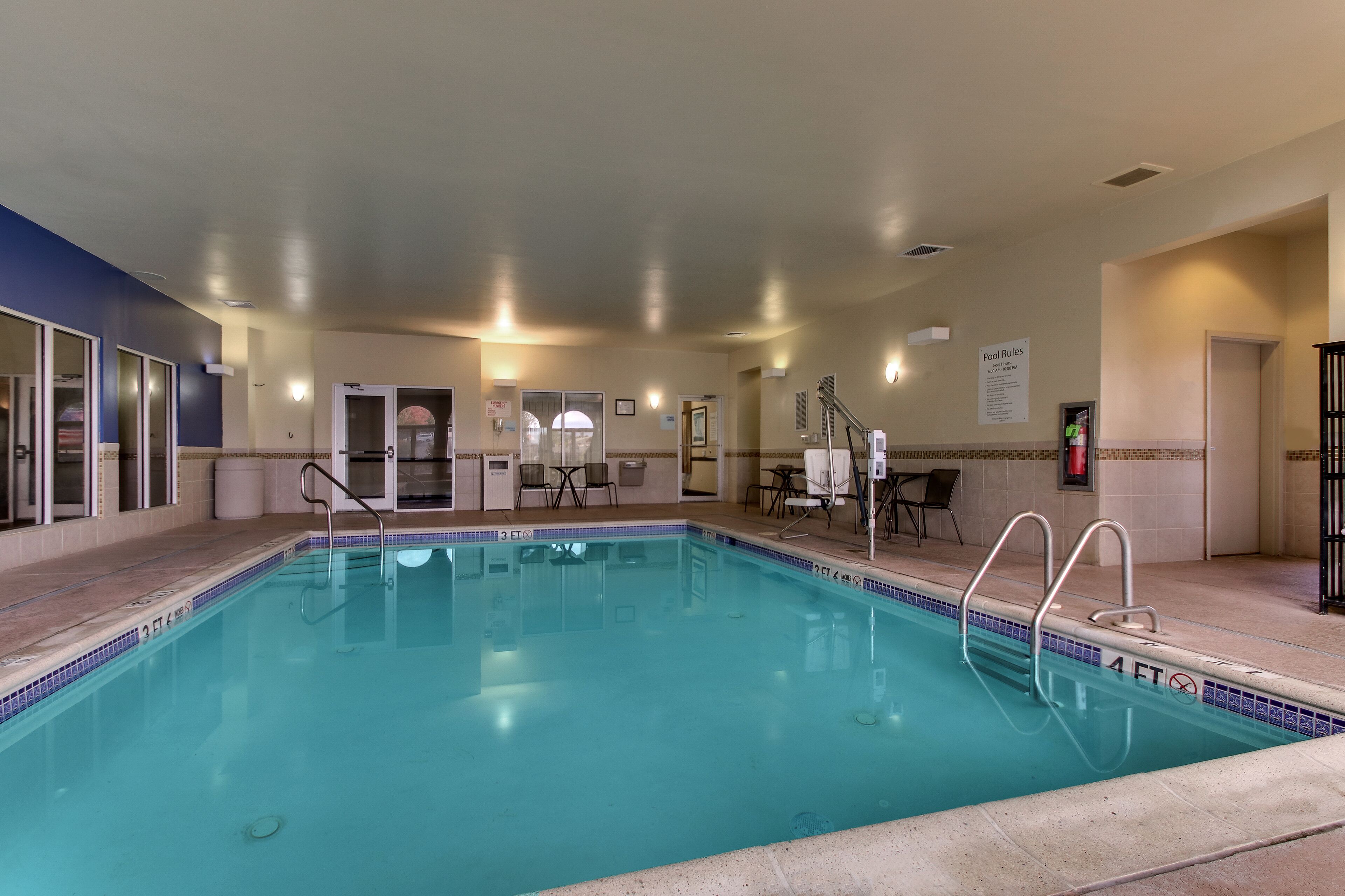 A swimming pool with a 4 ft depth marker, poolside chairs, and a 'Pool Rules' sign.