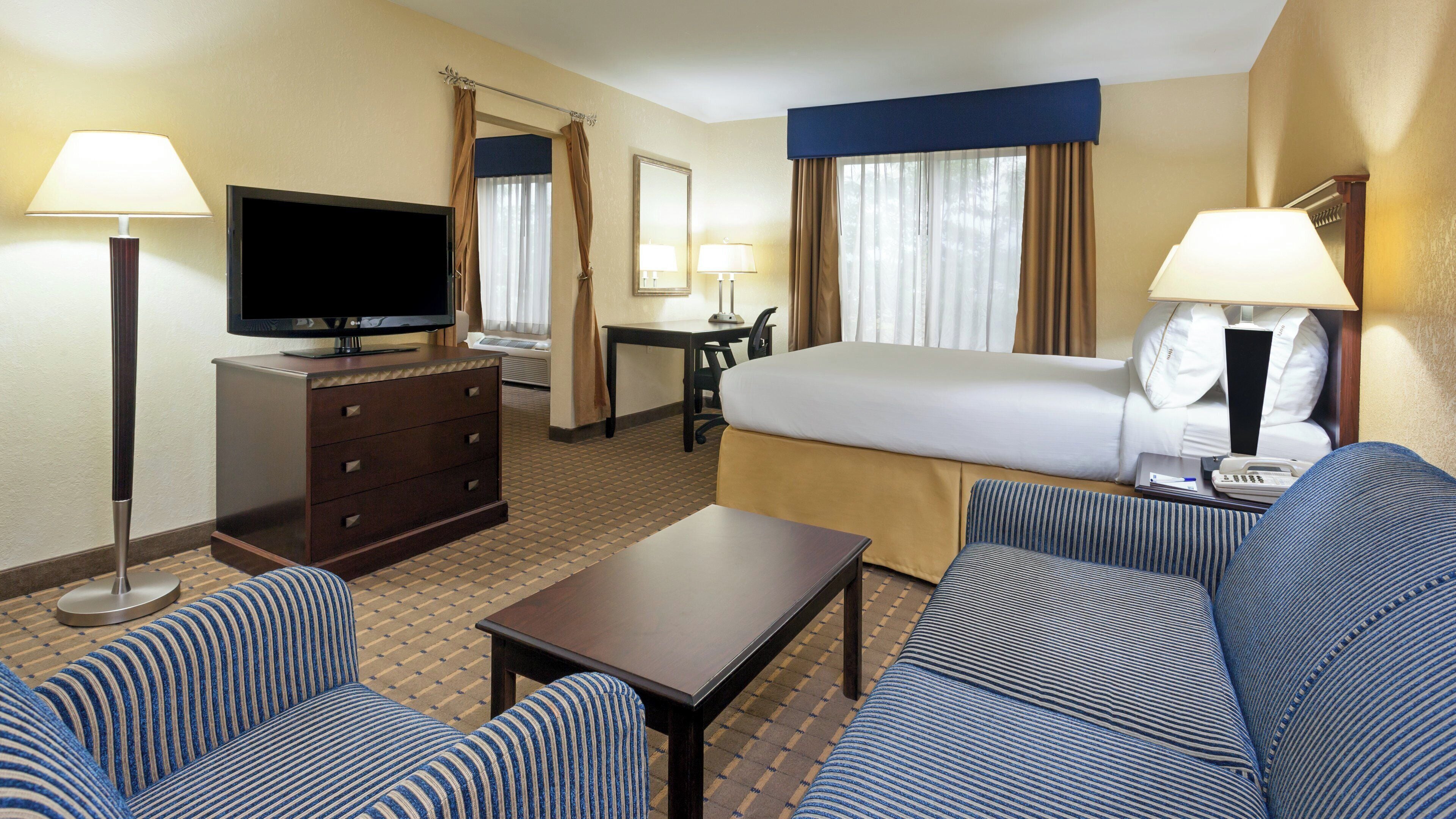 Una habitación de hotel con cama, escritorio, televisor, sofá y mesa de centro.