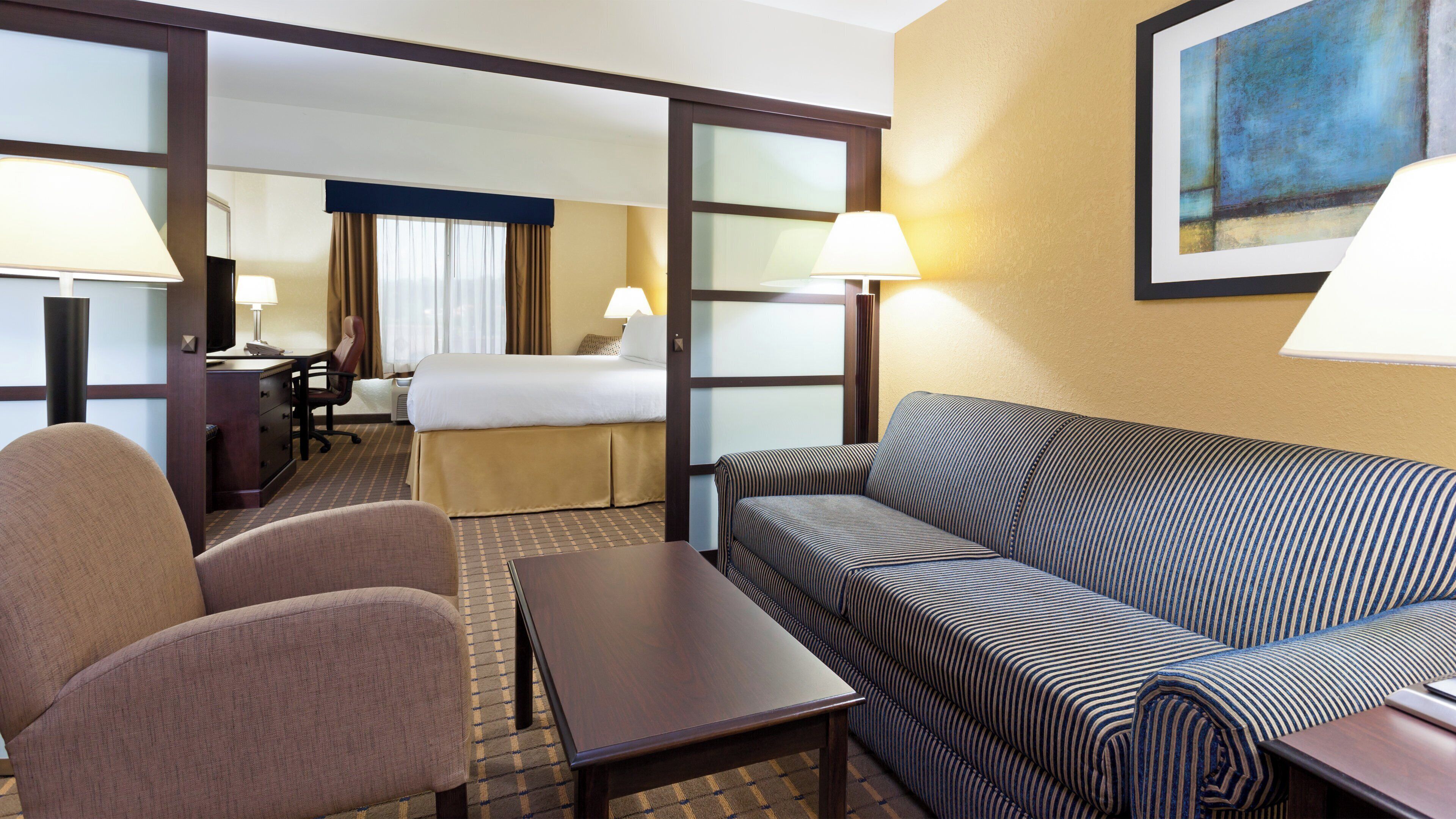 A hotel room with a bed, two armchairs, a sofa, a desk, and a lamp.