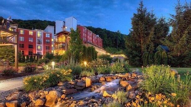 A hotel with multiple red buildings, a landscaped garden with a small stream, and a forested hillside in the background. - Holiday Inn Express & Suites Allentown West by IHG (Allentown)