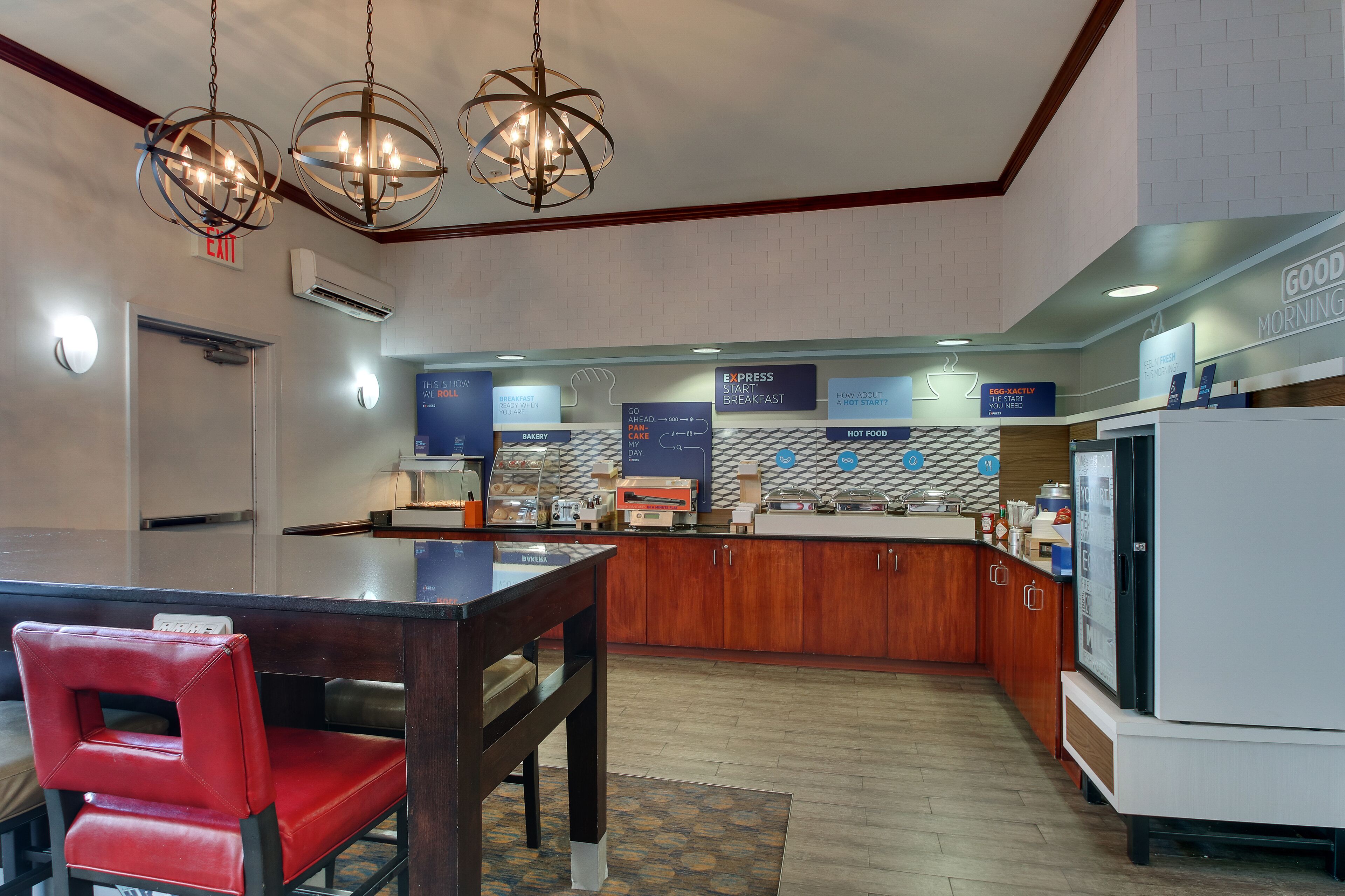 A hotel breakfast area with a wooden counter, a red chair, and a chandelier.