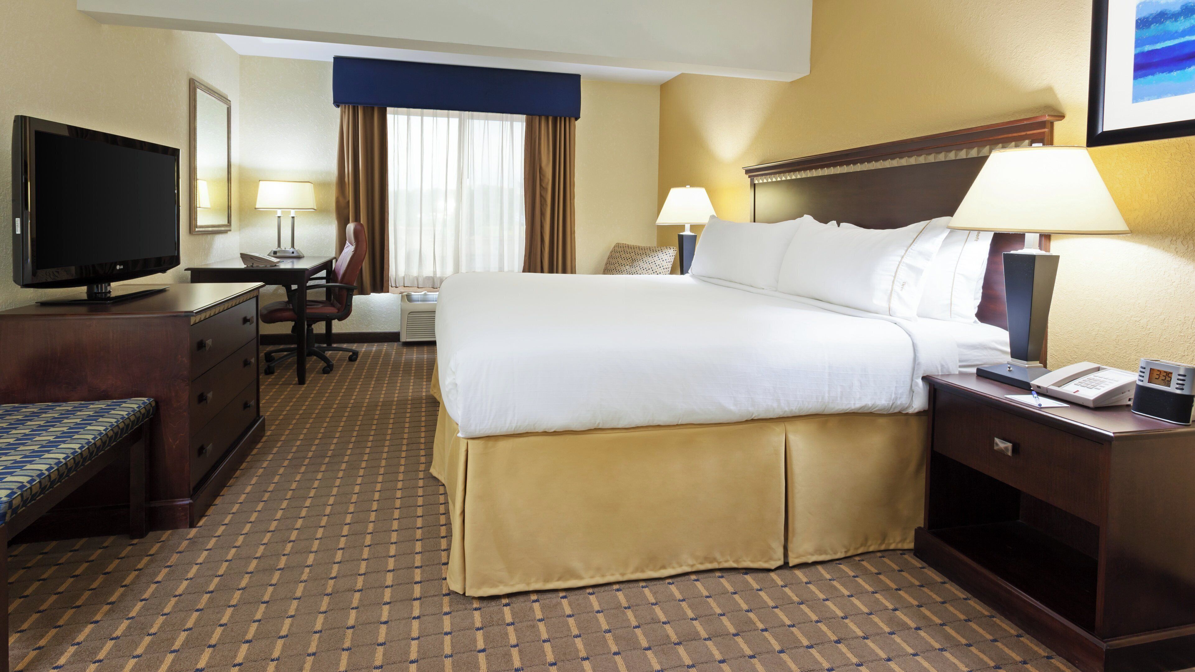 Ein Hotelzimmer mit Bett, Schreibtisch, Stuhl, Fernseher, Lampen und einer Uhr.