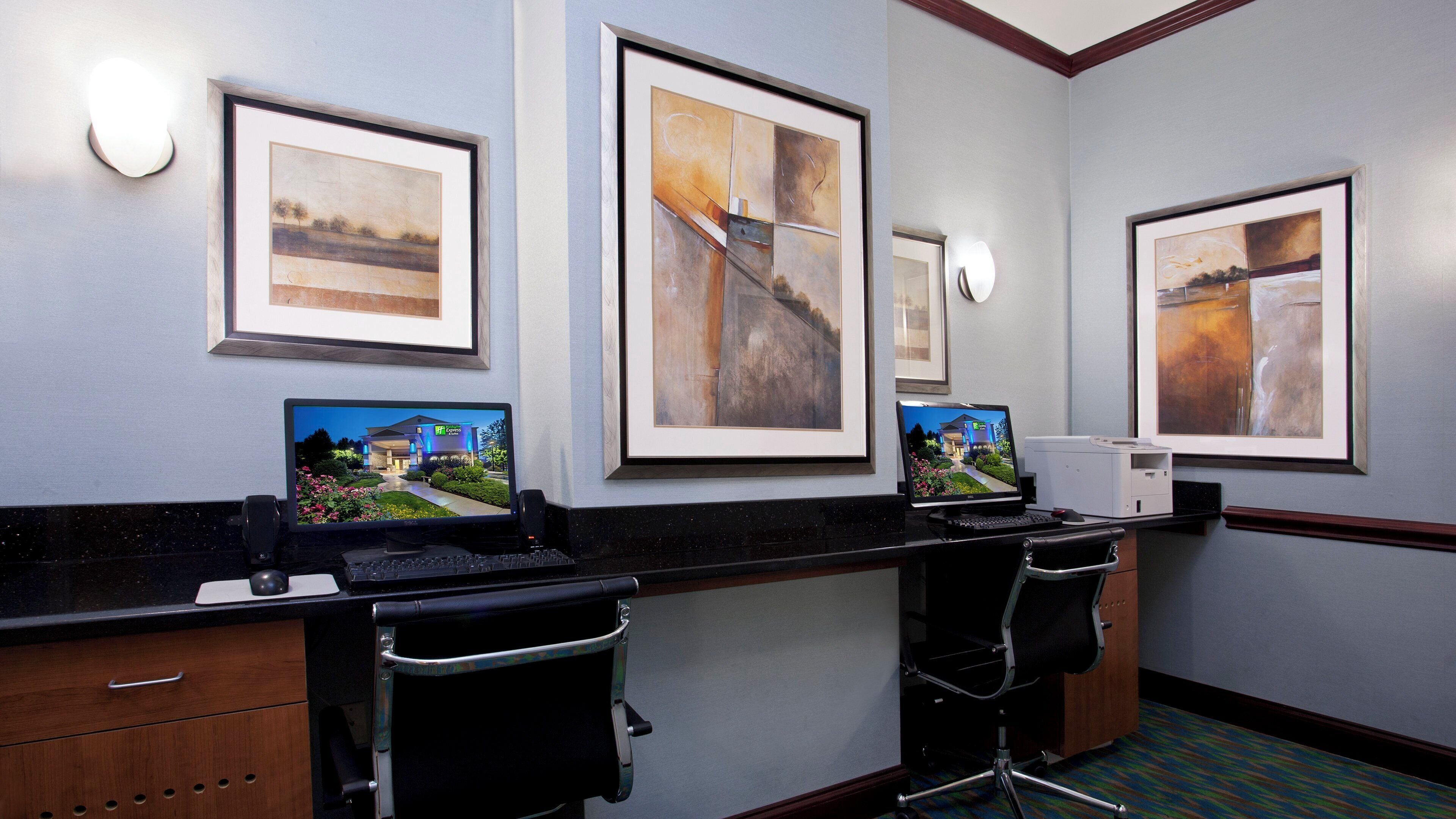 A hotel reception desk with framed artwork on the walls, a desktop computer, and a laptop.