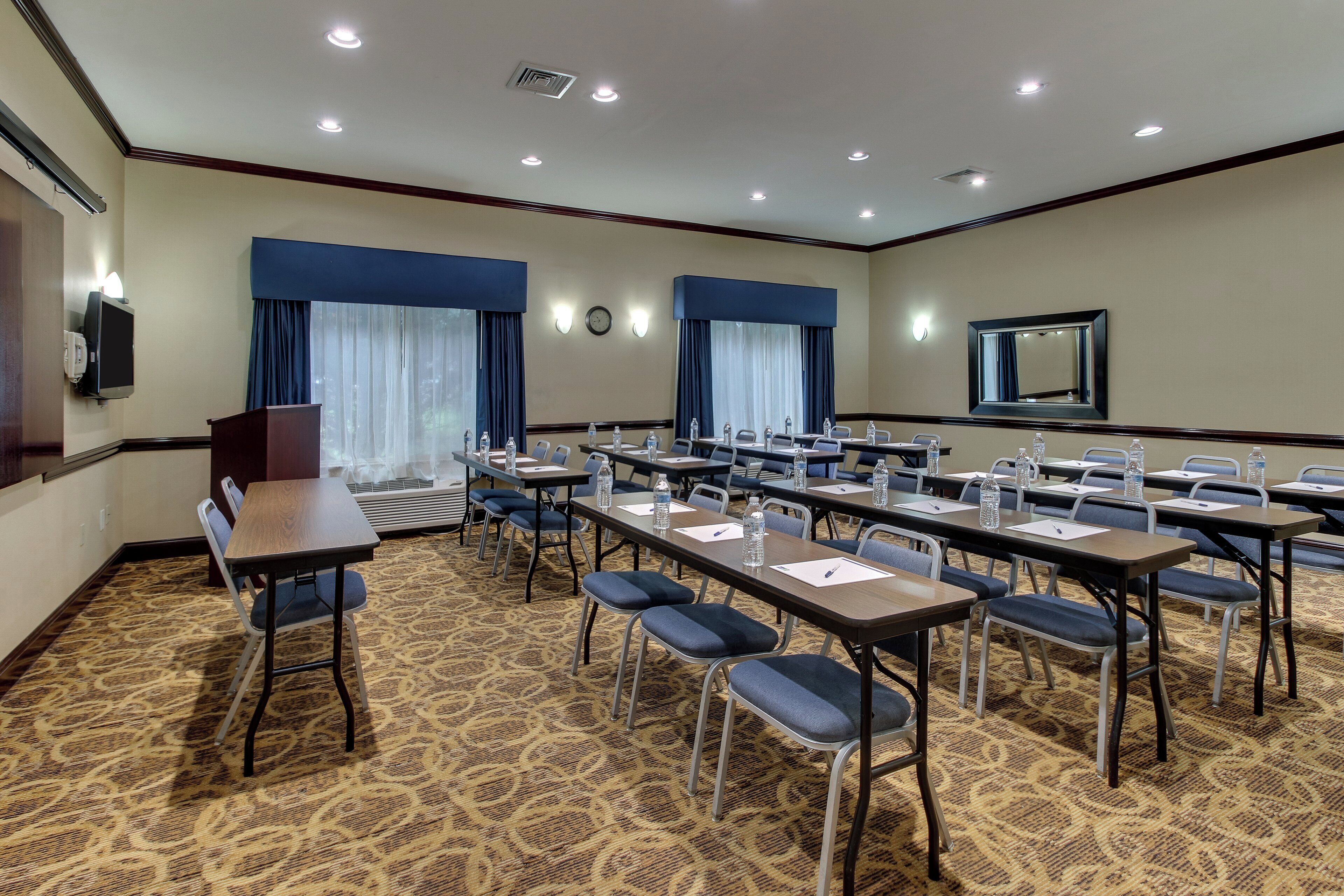 A conference room with multiple tables and chairs, equipped with water bottles and pens, and a clock on the wall.