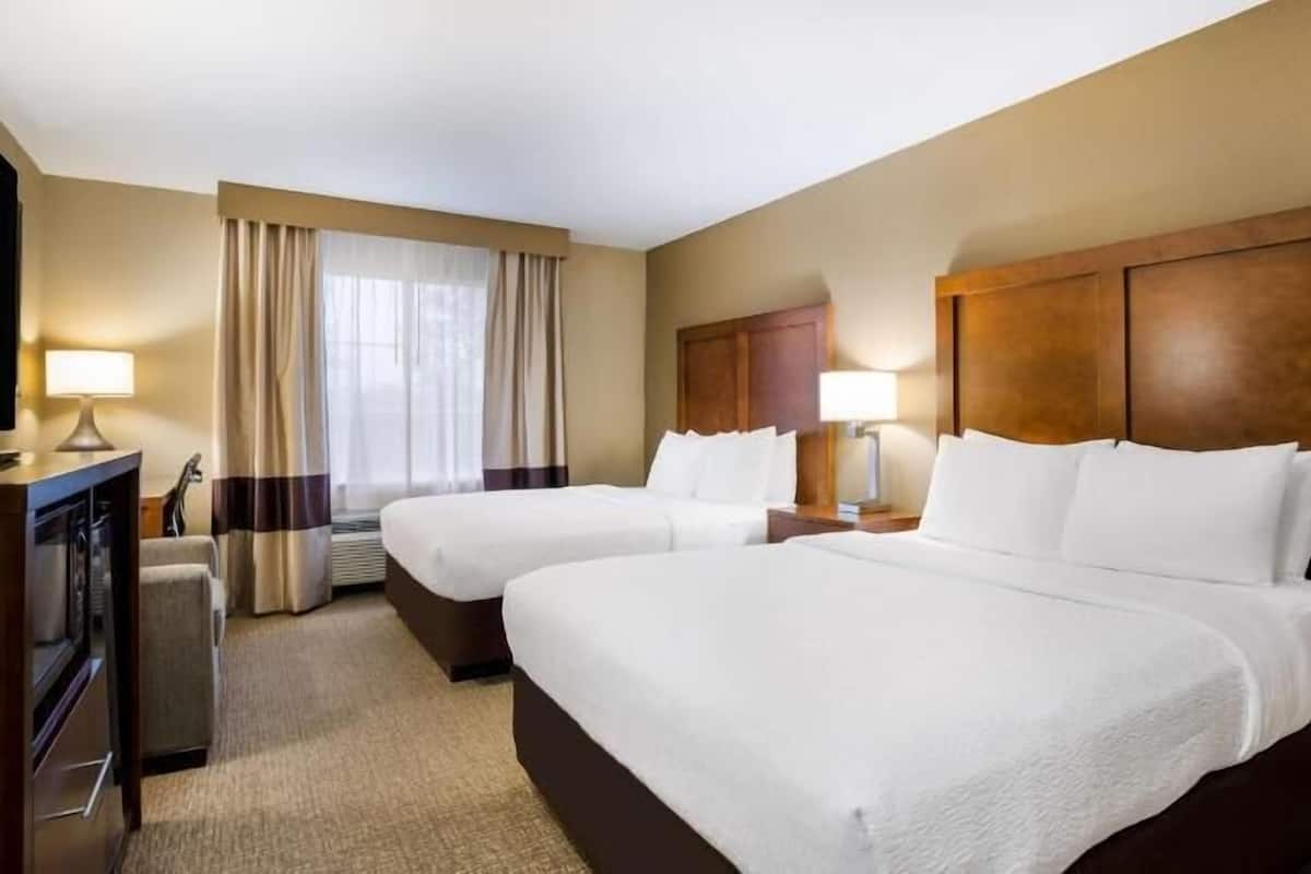 Una habitación de hotel con dos camas, un televisor y un escritorio con lámpara.