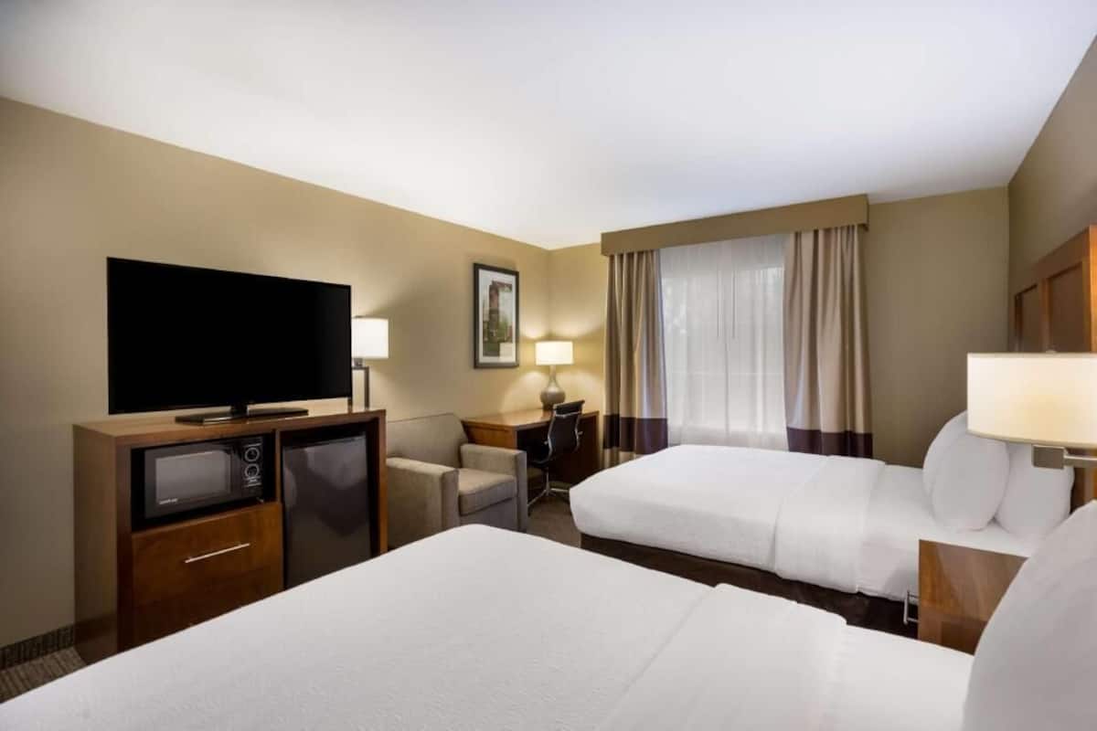 Habitación de hotel con dos camas, televisión, escritorio con lámpara, microondas y refrigerador pequeño.