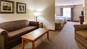 Une chambre d’hôtel avec un canapé, une petite table, une lampe, une télévision et un lit avec deux oreillers.