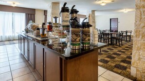 Un espace dédié au petit-déjeuner dans l’hôtel, aménagé avec un buffet proposant une variété d’aliments, ainsi qu’un coin café et différents récipients pour servir les aliments.