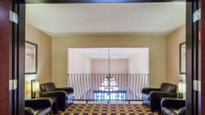 Un hall d’hôtel avec un sol à carreaux, deux fauteuils en cuir, un luminaire suspendu et une grande fenêtre.