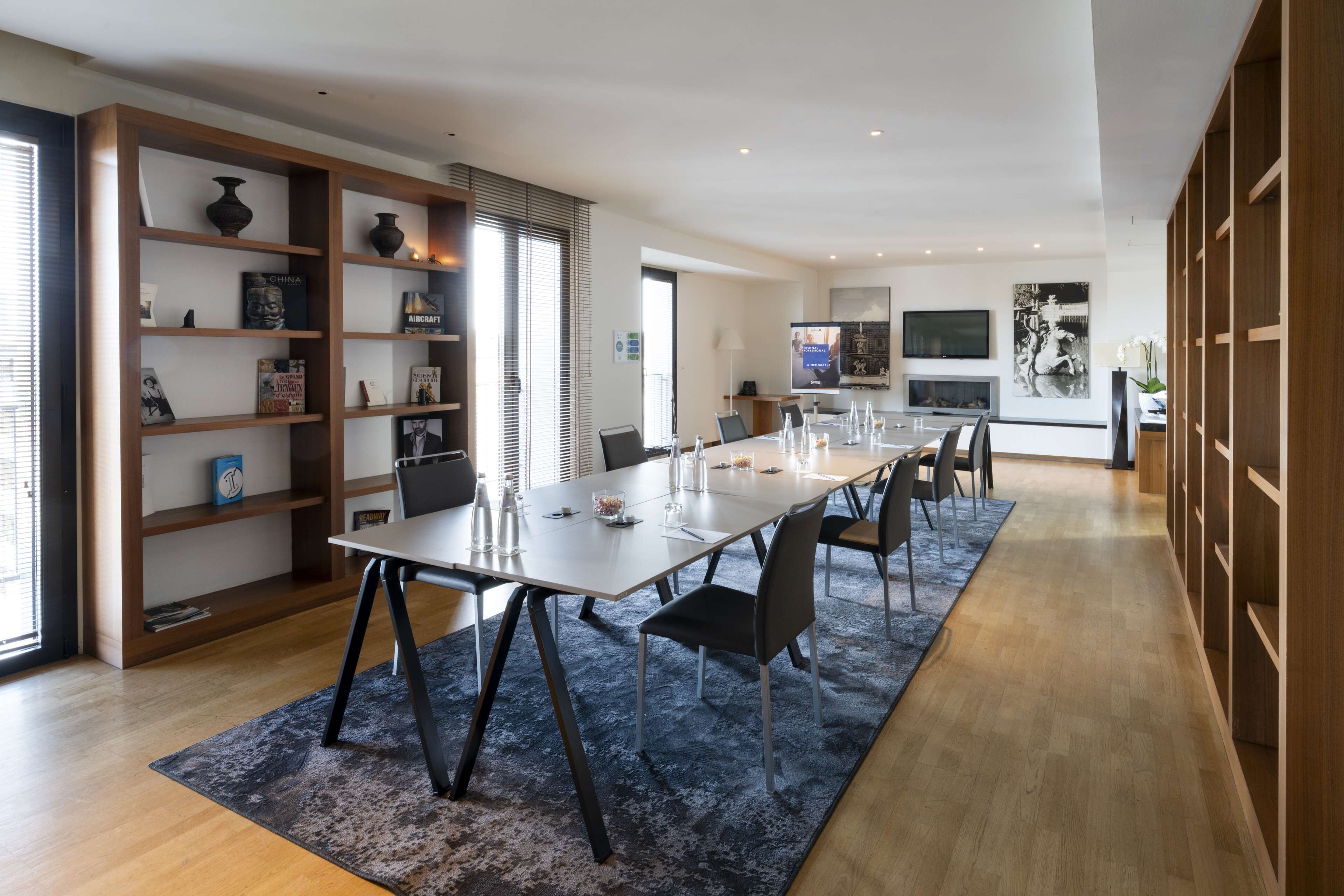Uma sala de jantar moderna com uma mesa comprida, cadeiras e uma estante de livros.