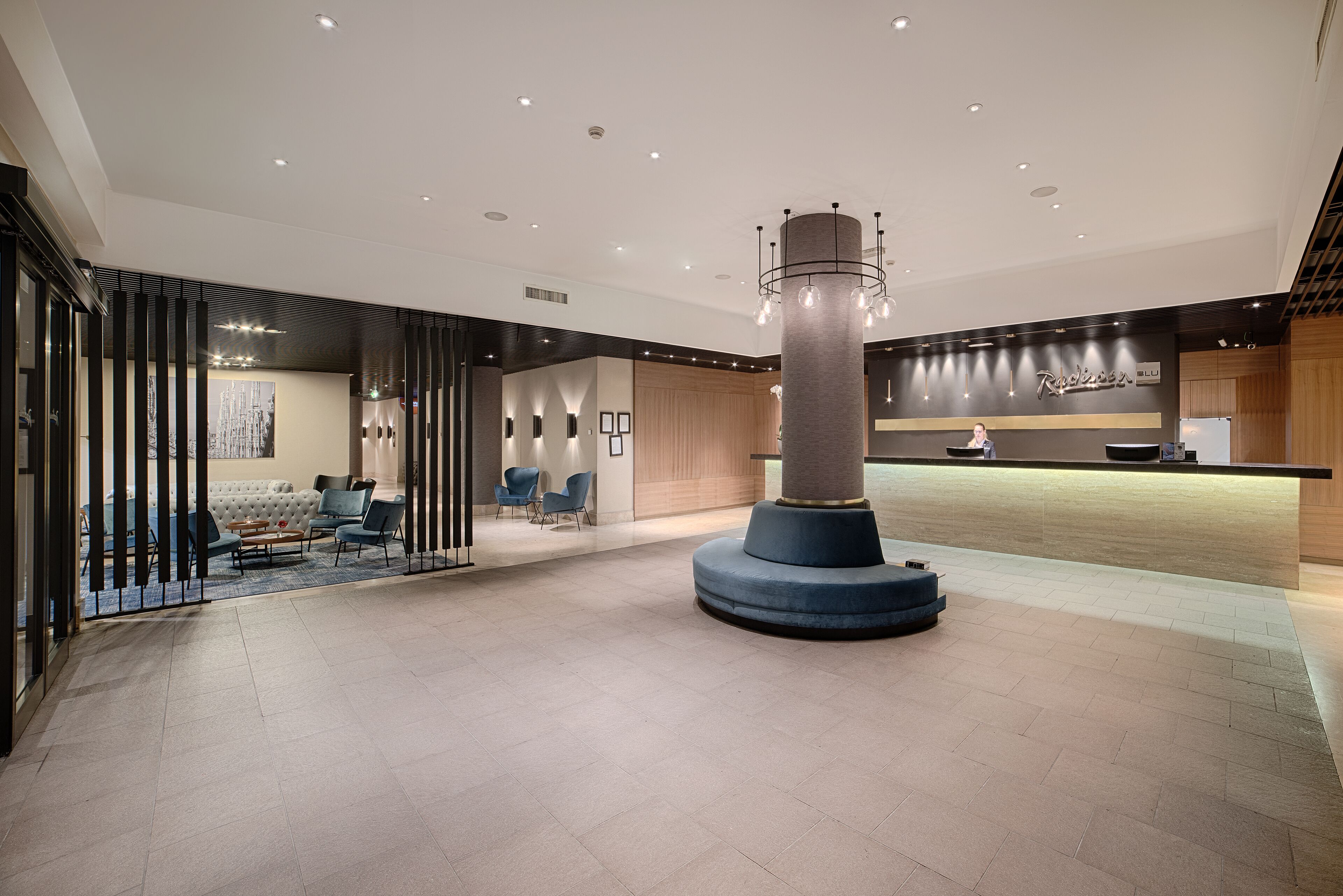 Een moderne lobby met een centrale pilaar, een zithoek en een receptiebalie.