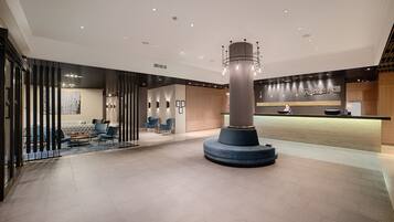 Een moderne lobby met een centrale pilaar, een zithoek en een receptiebalie.