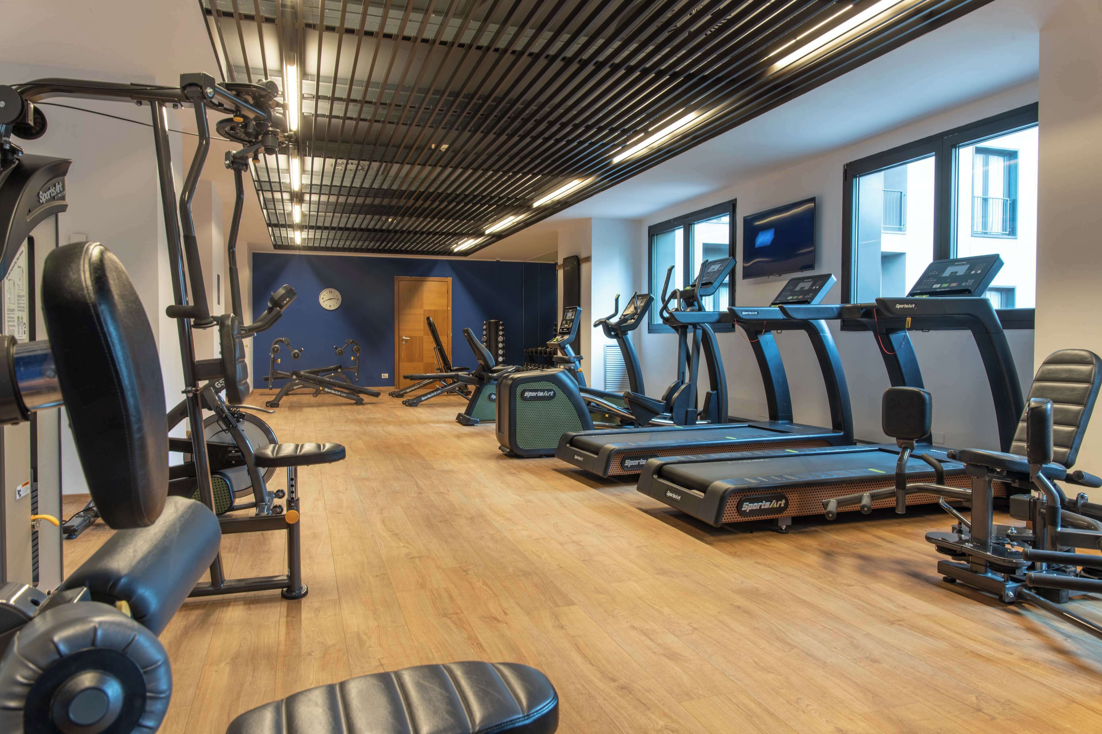 A gym with treadmills, weight machines, and a wooden floor.