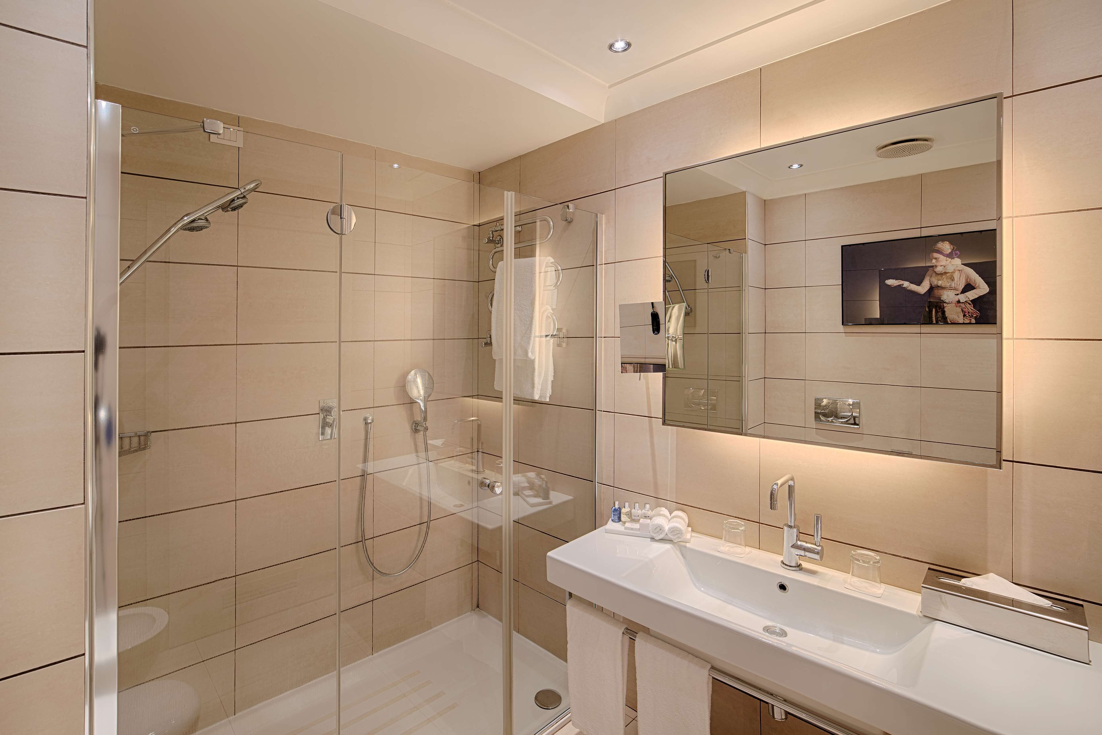 Un bagno moderno con cabina doccia in vetro, uno specchio grande e un lavandino bianco con mobile contenitore.