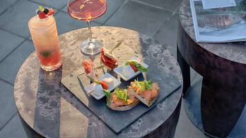 A round table with a variety of food items and drinks, including a tall glass of iced beverage, a cocktail, and several small plates with appetizers.