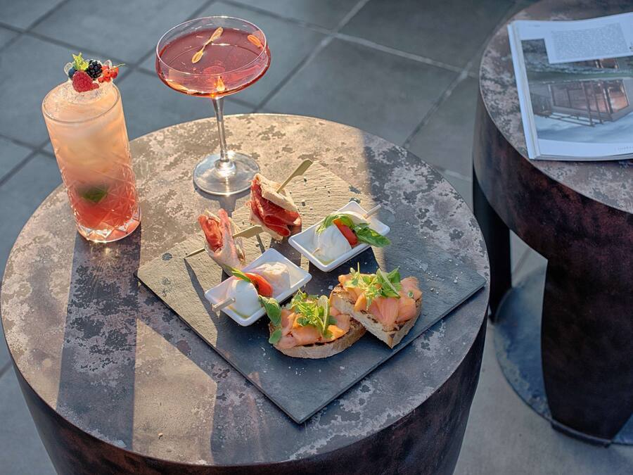 A round table with a variety of food items and drinks, including a tall glass of iced beverage, a cocktail, and several small plates with appetizers.