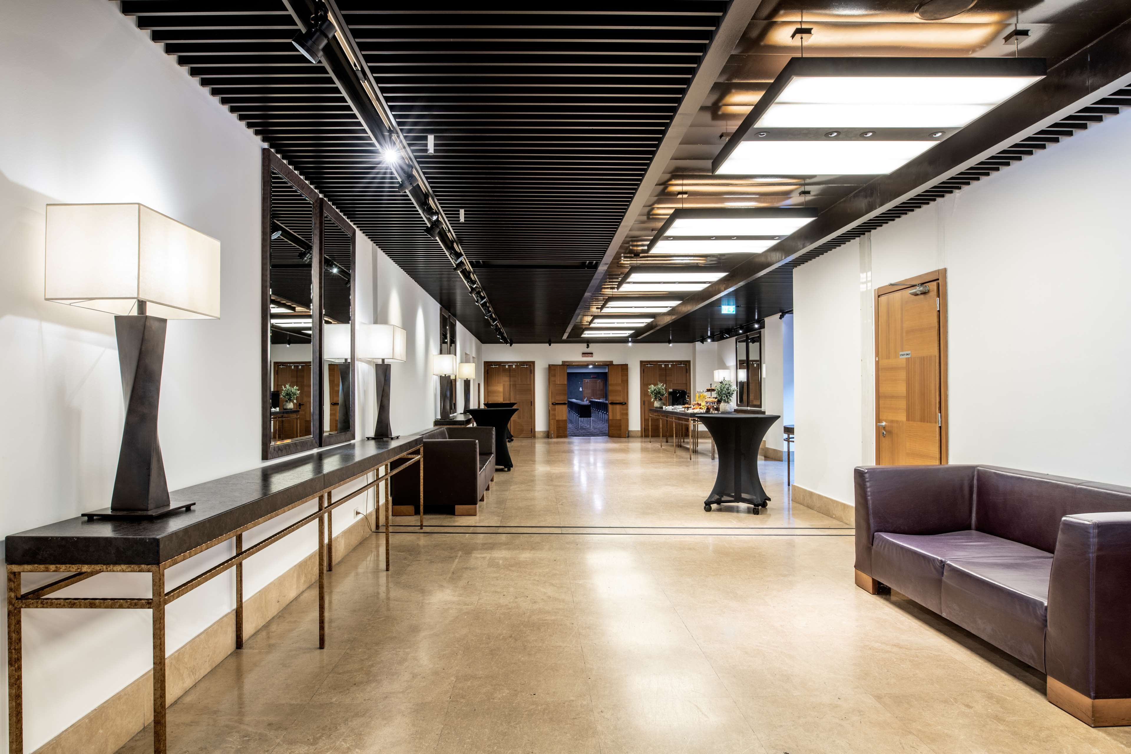 A modern hallway with a long reception desk, a sofa, and a table with a lamp.