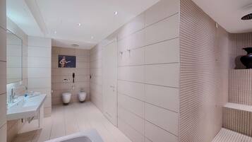 Een moderne badkamer met een badkuip, twee toiletten, een wastafel en een spiegel.