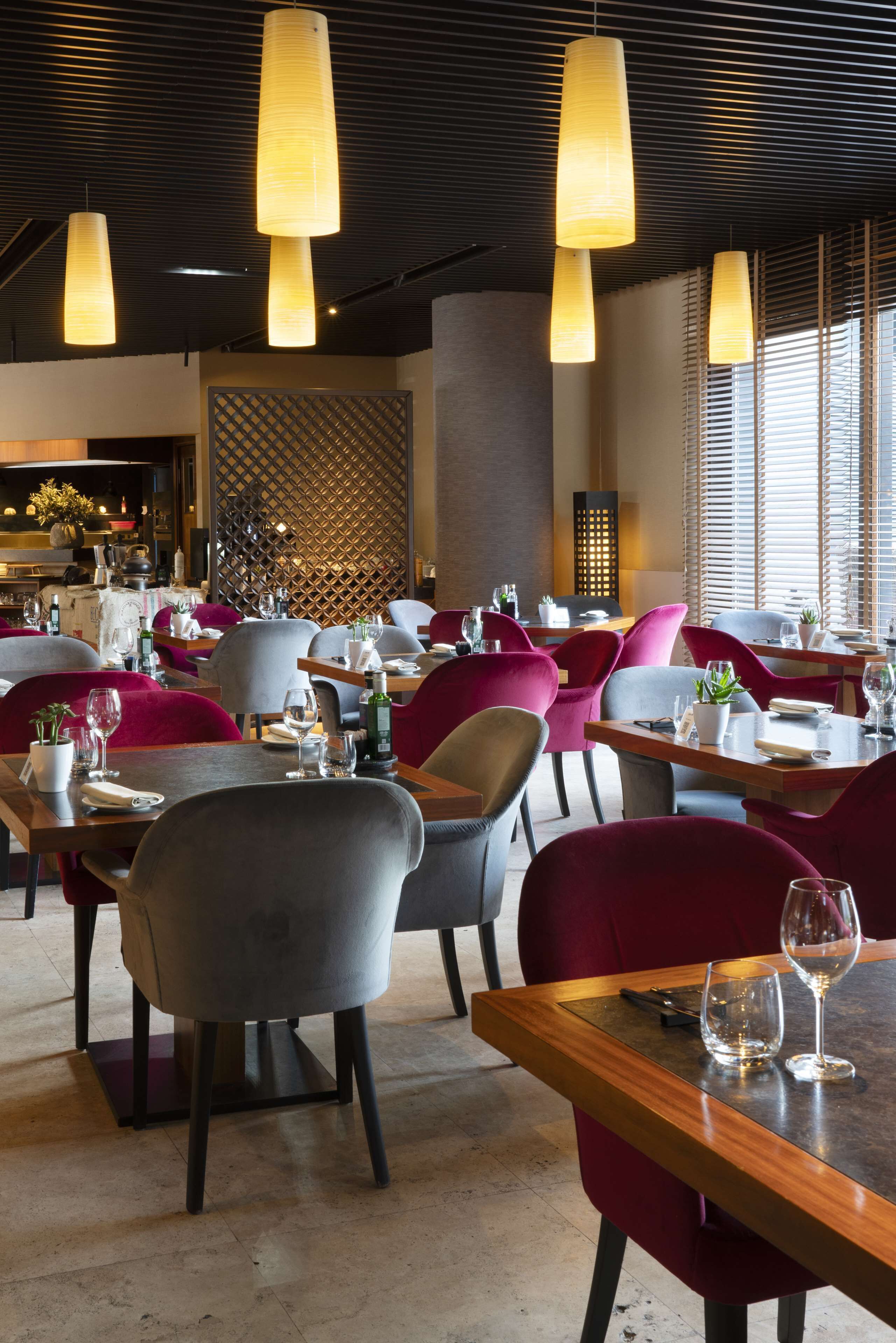 Interior de restaurante con varias mesas, sillas y lámparas colgantes.