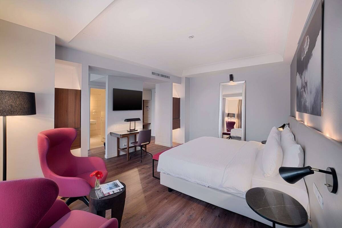A modern hotel room with a bed, a desk, a chair, and a TV.