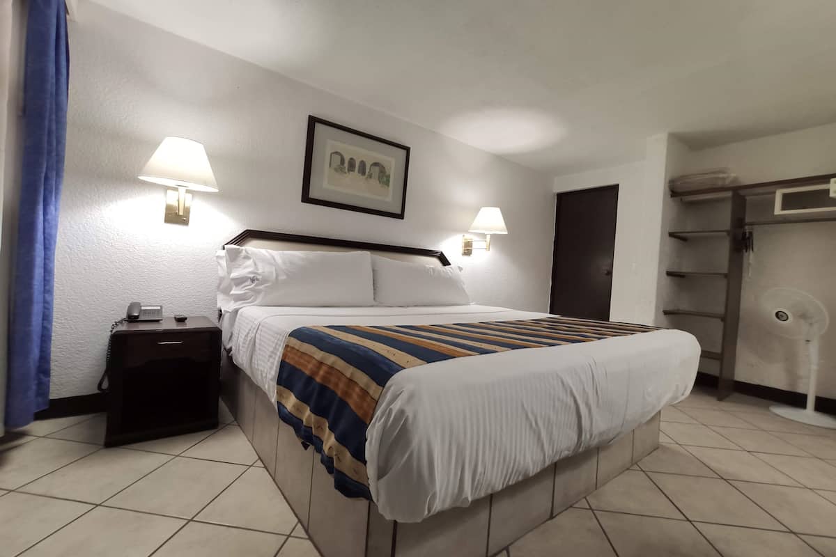 A hotel room with a bed, bedside lamps, a nightstand, a framed picture on the wall, and a wardrobe.