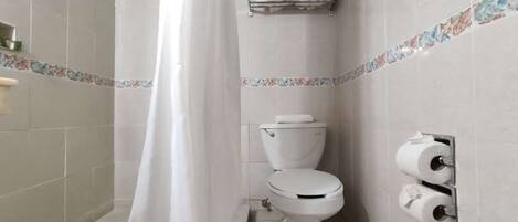 Een kleine, praktische badkamer met toilet, douchegordijn en toiletrolhouder.