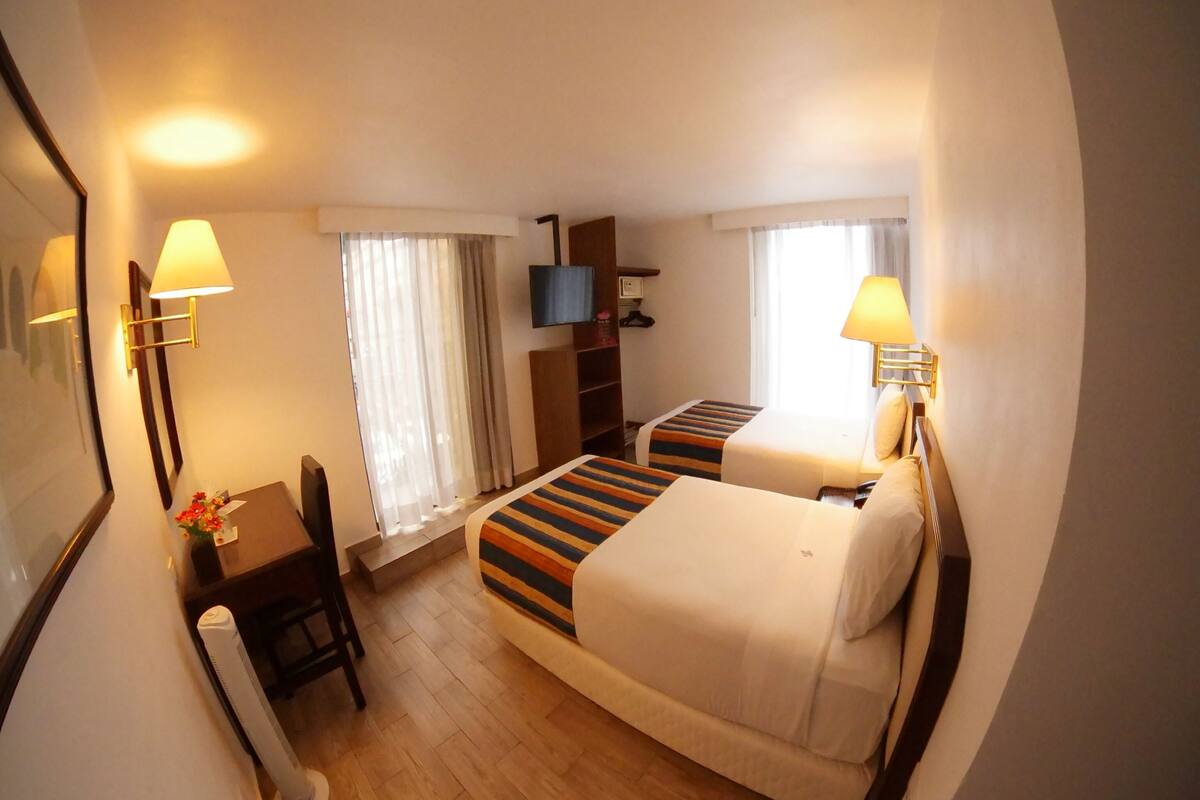 A hotel room with a bed, a desk, a chair, a TV, and a window with curtains.