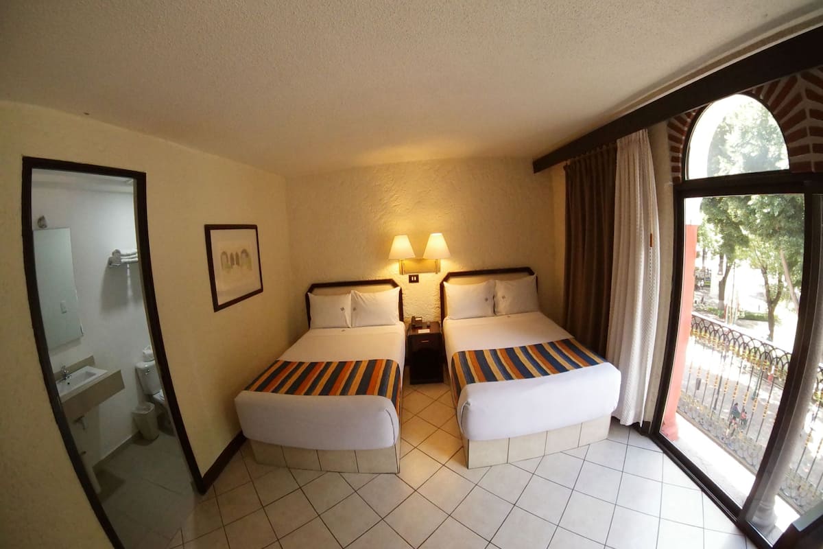 A hotel room with two beds, a bathroom, and a balcony with a view.
